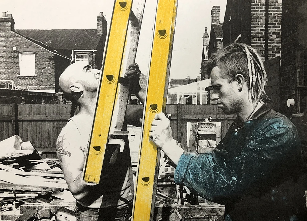 Two construction workers using a yellow ladder, urban brick building background, home renovation scene