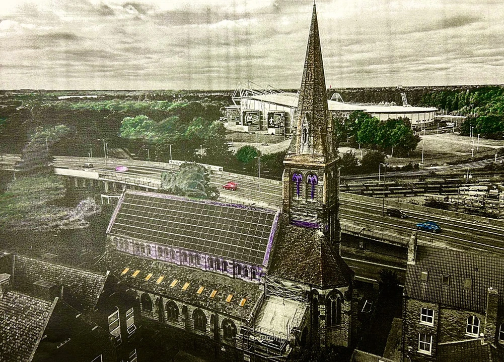 Historic church with tall spire near modern stadium, aerial view showing urban landscape with roads and trees