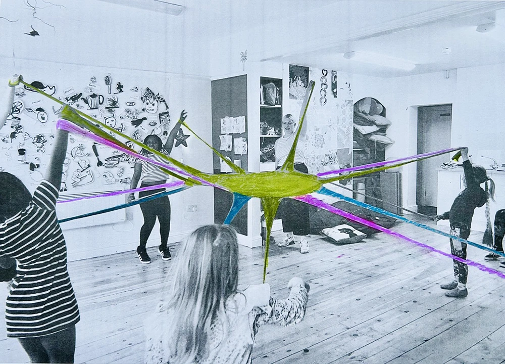 Art installation with colorful suspended star-like sculpture connecting multiple people in a white gallery space with wooden